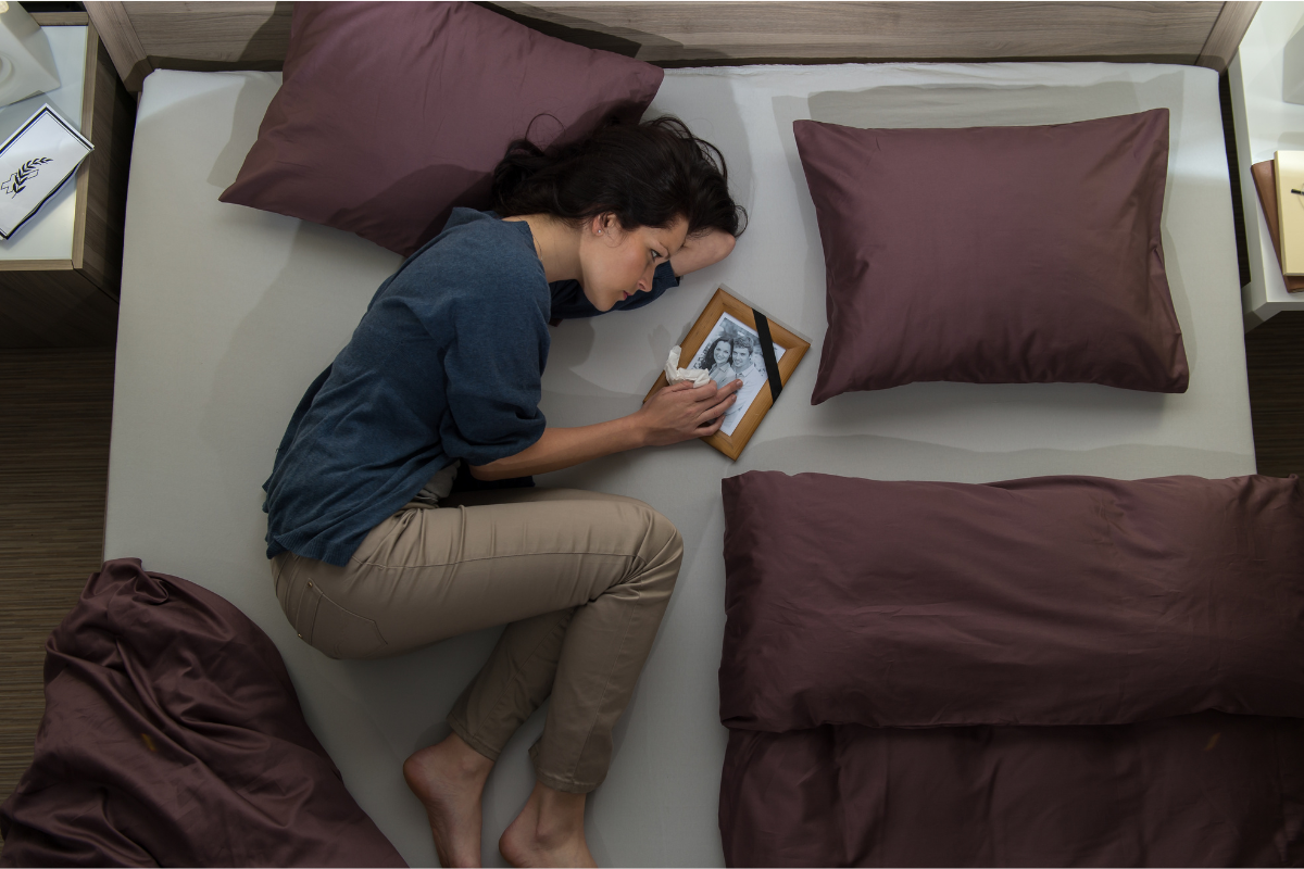 Image of a woman curled up on a bed looking a photo of she and her husband before he passed away.