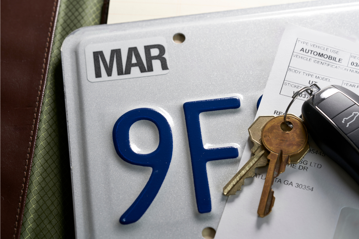 Image of a license plate, a car registration, and a key fob with other keys on a desktop for a blog post covering how to report a death to the DMV.
