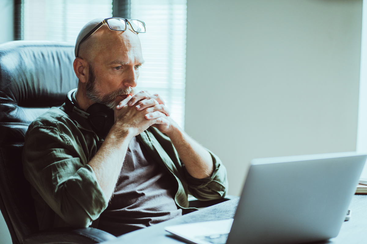 Image of a man thinking while looking at an open laptop.