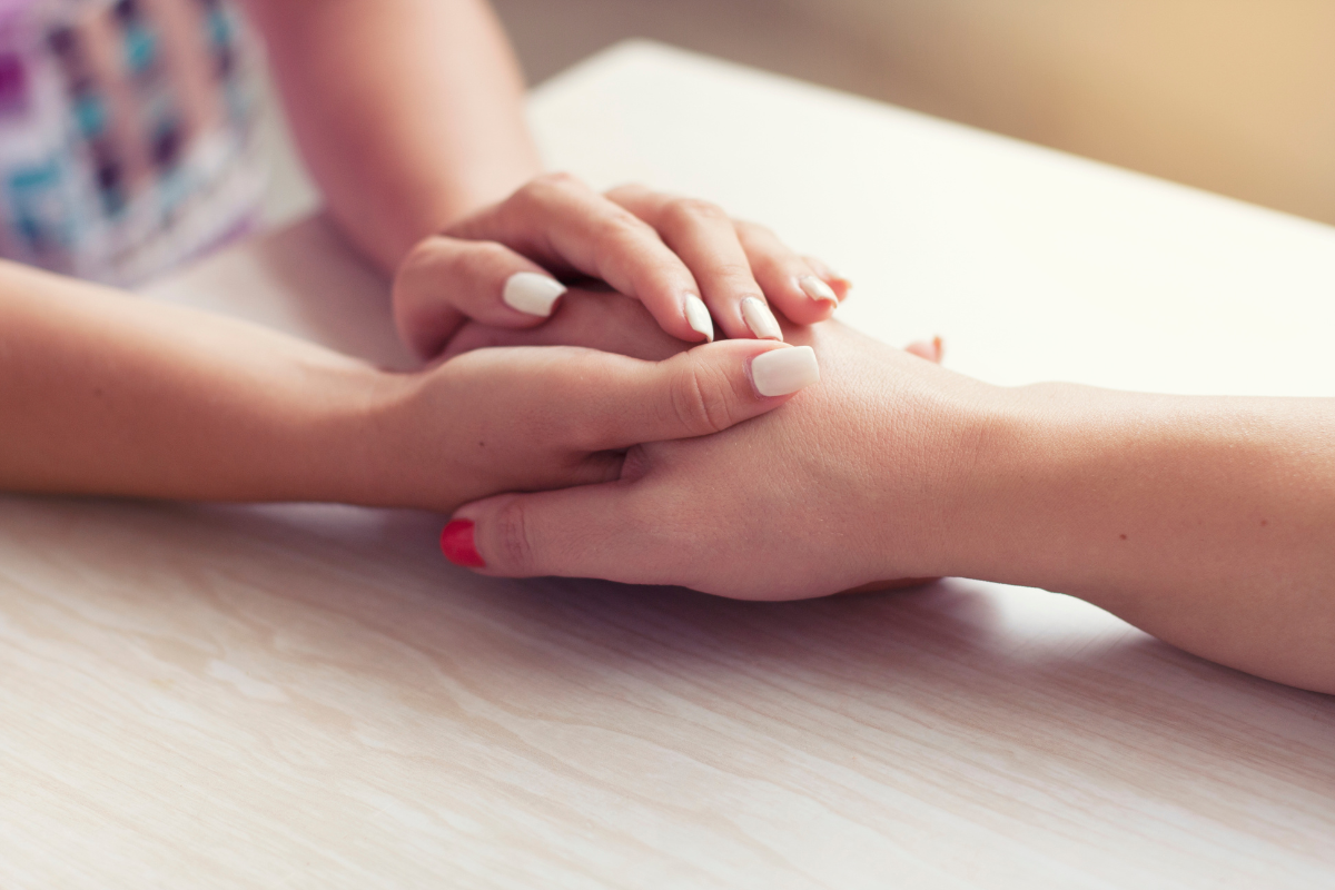 Image of a woman holding the hand of another for a blog post about helping a loved one through loss.