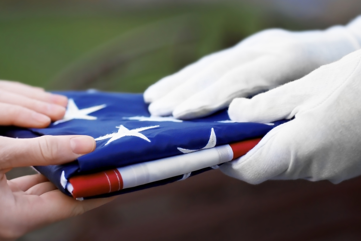 Image of a folded American flag being handed to a surviving loved one for a blog post covering how to notify DFAS of a death.